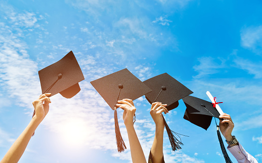 Four hands holding graduation hats on background of blue sky.